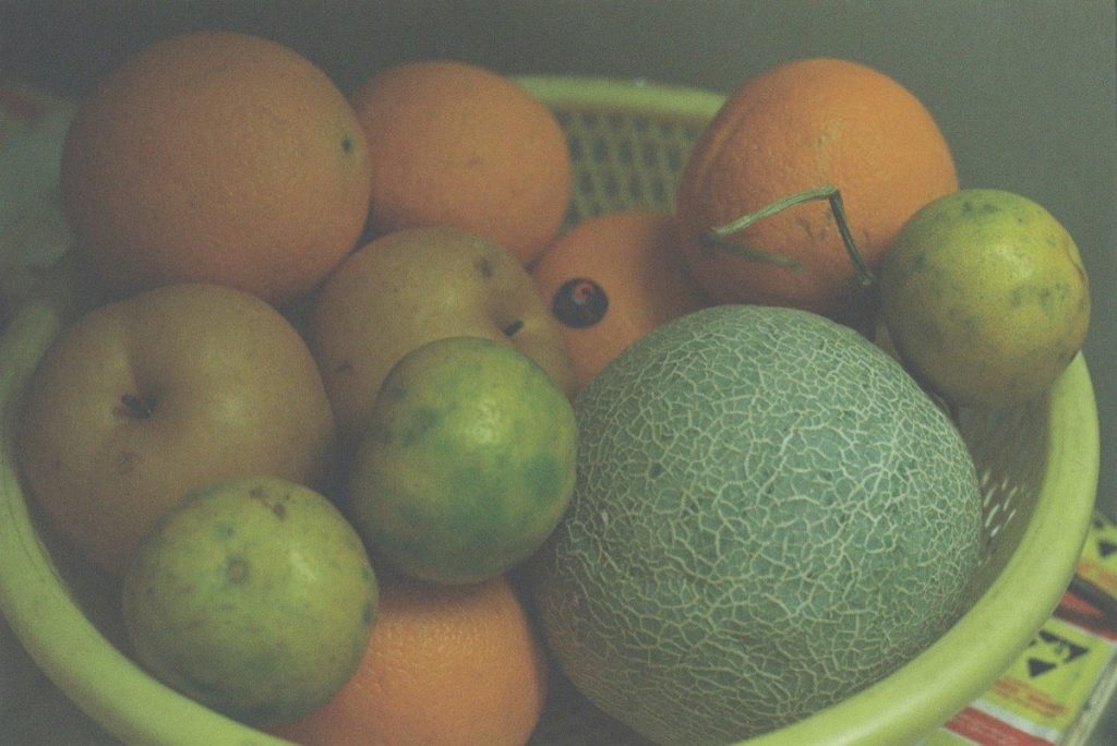 Bol vert rempli de fruits frais variés, agrumes, kiwi et baies, sur une table en bois avec lumière naturelle