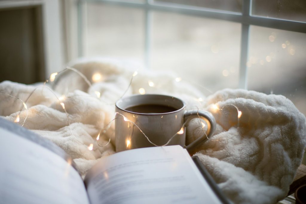 Tasse de café et livre sur un plaid, lumière du matin, ambiance cocooning hivernale