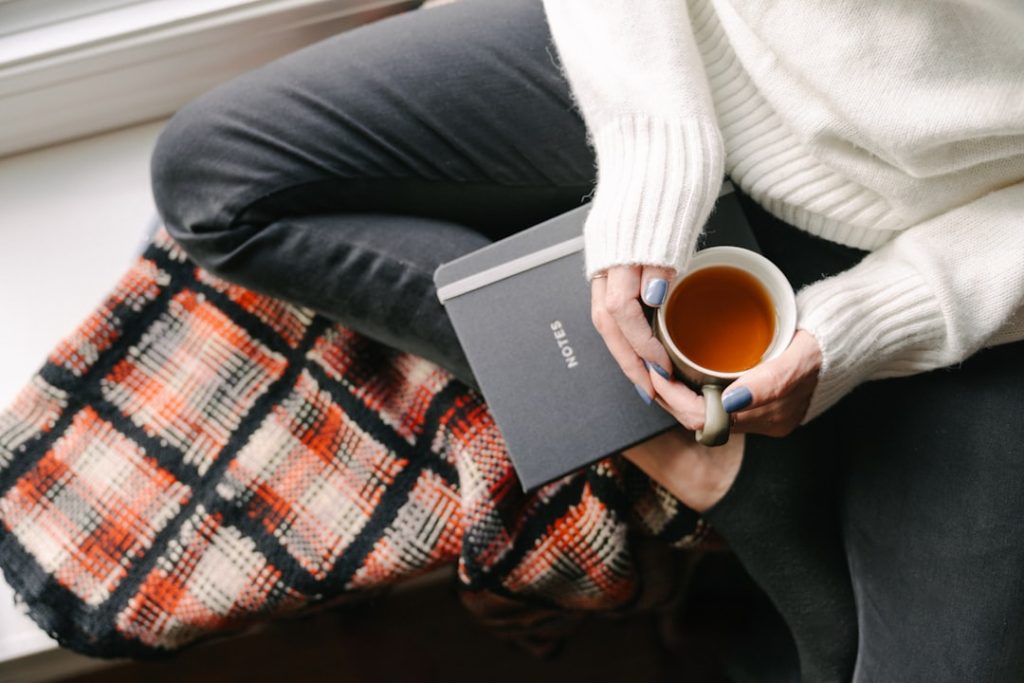 Femme assise sur le rebord d une fenêtre tenant une tasse de tisane, un moment de pause pour gérer son stress