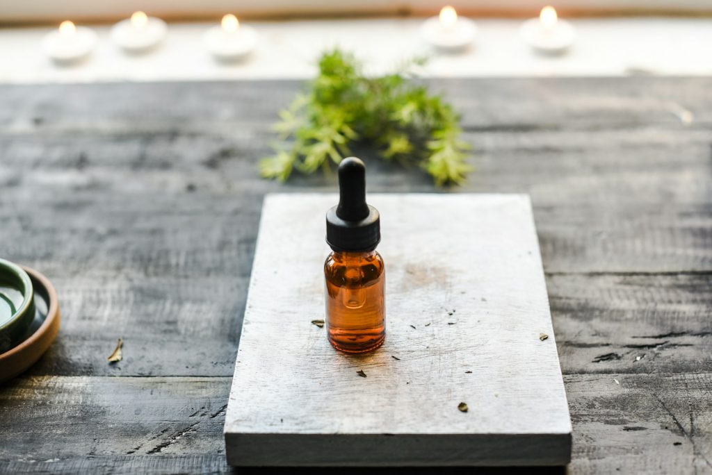 Flacon d'huile essentielle avec compte-gouttes posé sur un plateau en bois, à la lumière de bougies