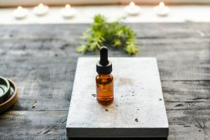 Flacon d'huile essentielle avec compte-gouttes posé sur un plateau en bois, à la lumière de bougies