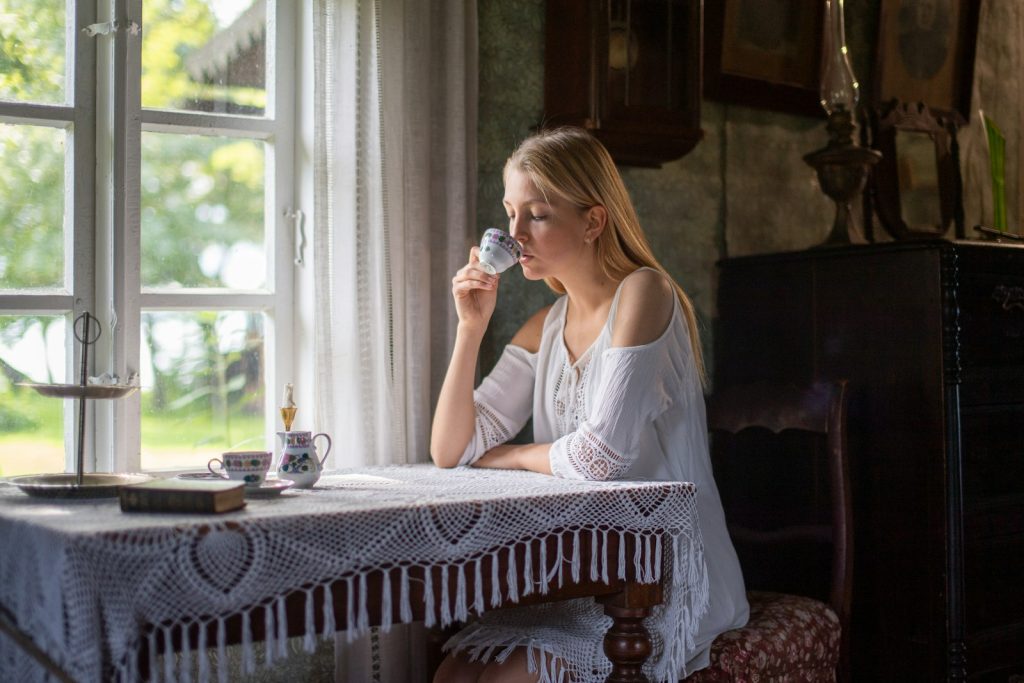 Jeune femme buvant une tisane pres d une fenetre en pleine lumiere du matin