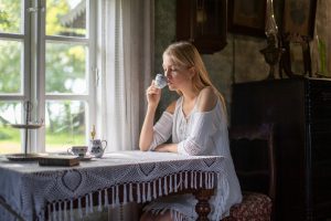Jeune femme buvant une tisane pres d une fenetre en pleine lumiere du matin